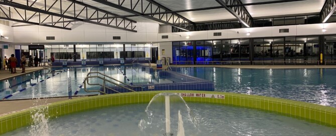 A photo of an indoor swimming pool, showing a water play area and 20m warm water pool
