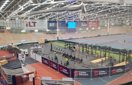 A photo of an indoor velodrome showing the track and a gym facility in the foreground